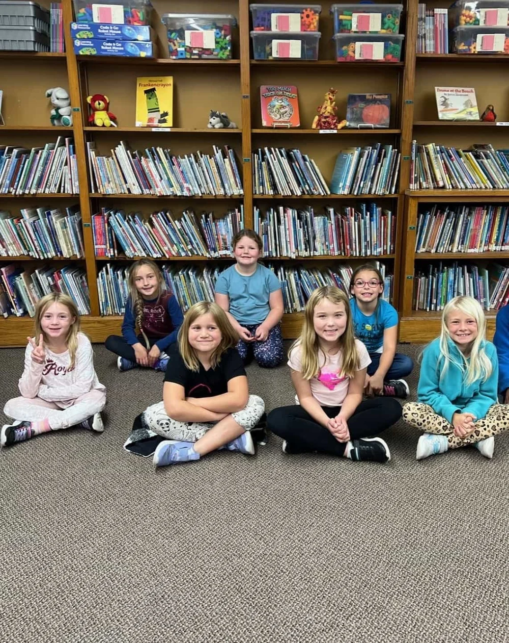 Seven children sitting together in front of their classroom library bookshelves.